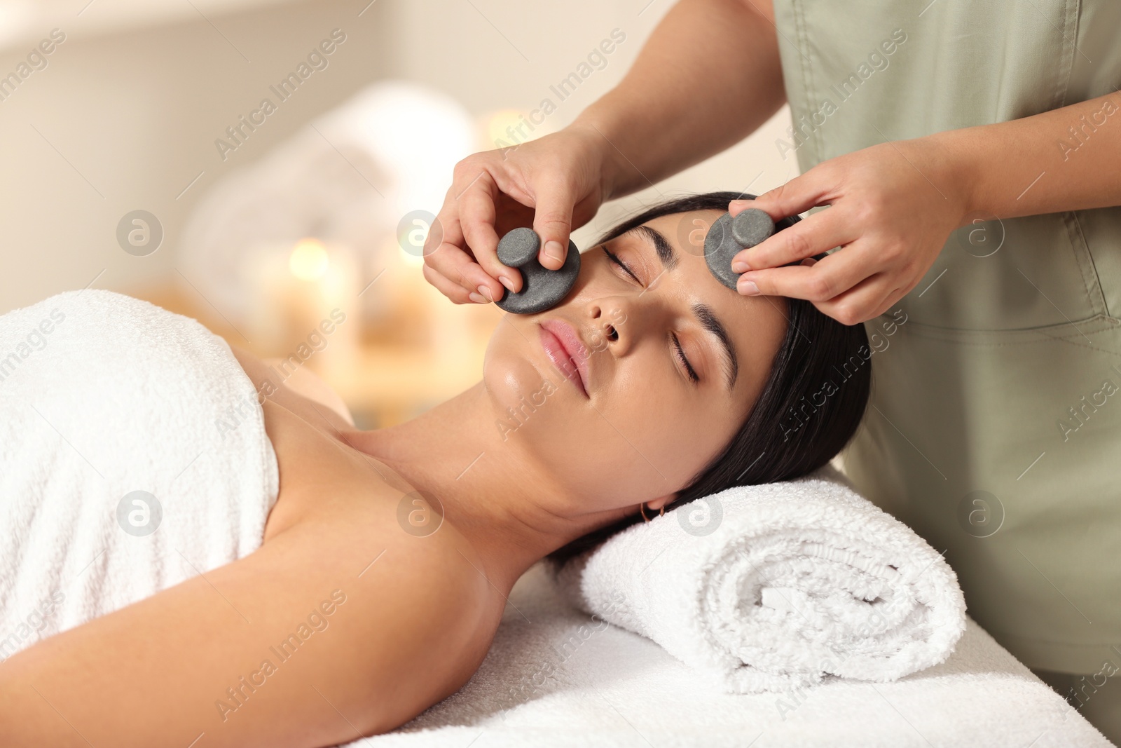 Photo of Young woman receiving facial massage with spa stones in salon