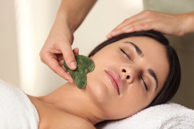 Photo of Young woman receiving facial massage with gua sha tool in spa salon