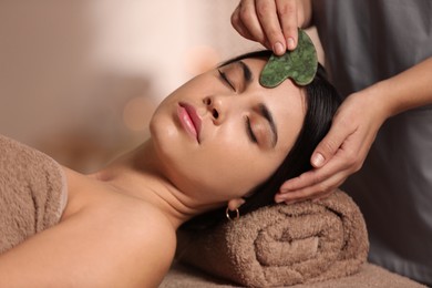 Photo of Young woman receiving facial massage with gua sha tool in spa salon