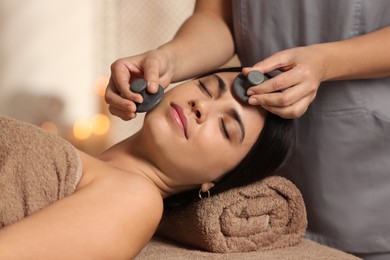 Photo of Young woman receiving facial massage with spa stones in salon