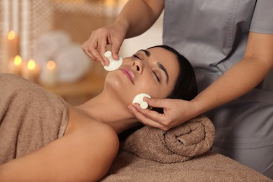 Photo of Young woman receiving facial massage with spa stones in salon