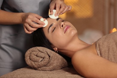 Photo of Young woman receiving facial massage with spa stones in salon