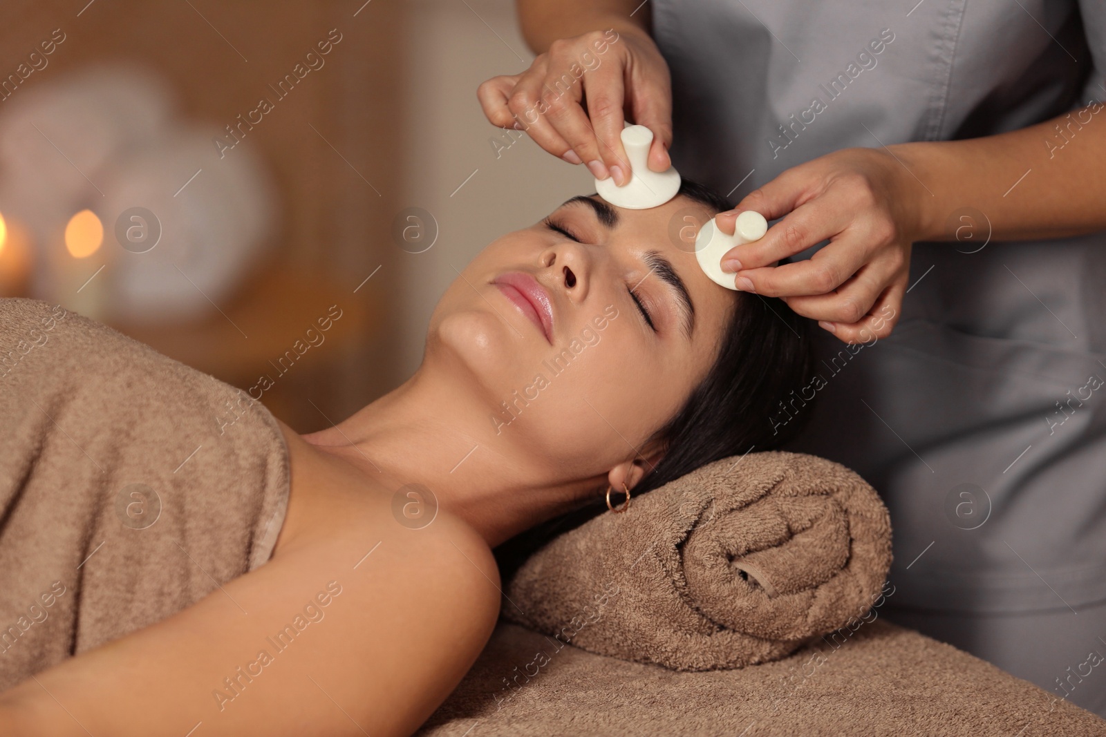 Photo of Young woman receiving facial massage with spa stones in salon