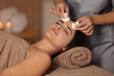 Photo of Young woman receiving facial massage with spa stones in salon