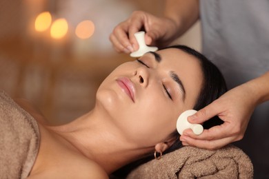 Photo of Young woman receiving facial massage with spa stones in salon