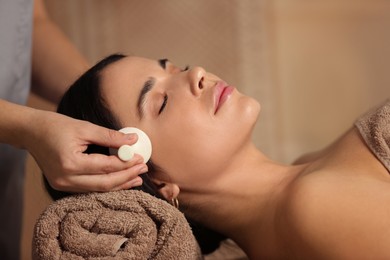 Photo of Young woman receiving facial massage with spa stone in salon