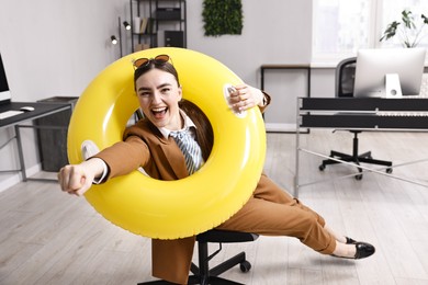 Photo of Businesswoman with inflatable ring and sunglasses posing on chair in office