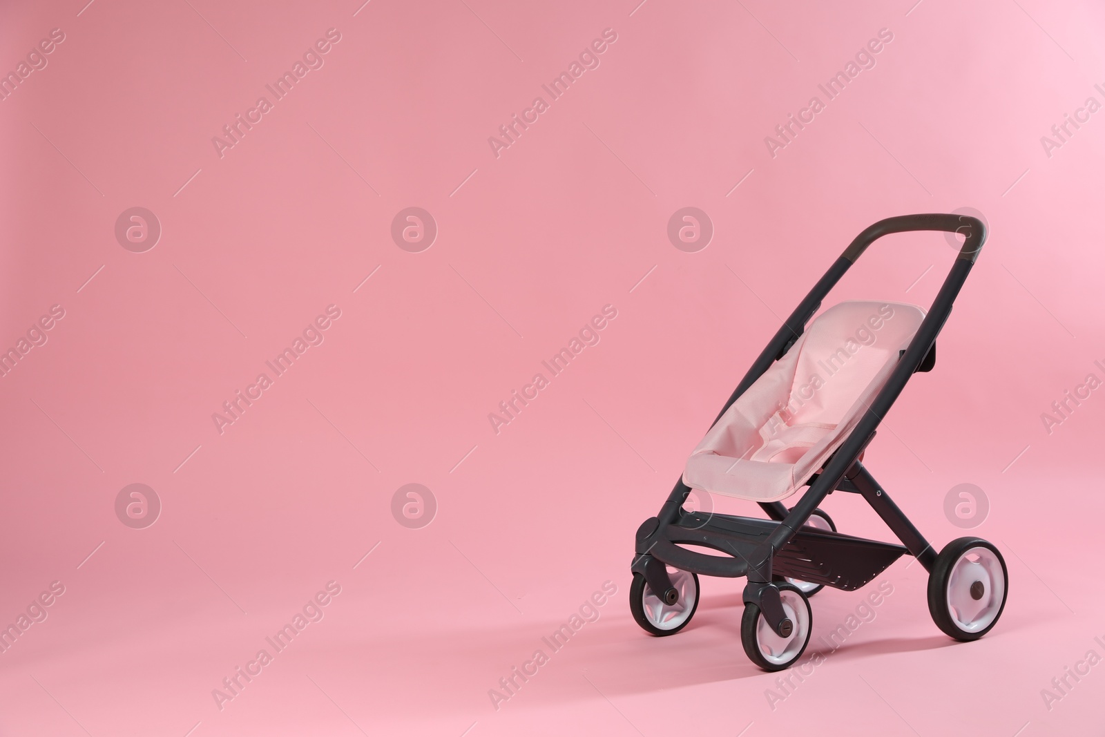 Photo of Stylish doll stroller on pink background, space for text. Kid's toy