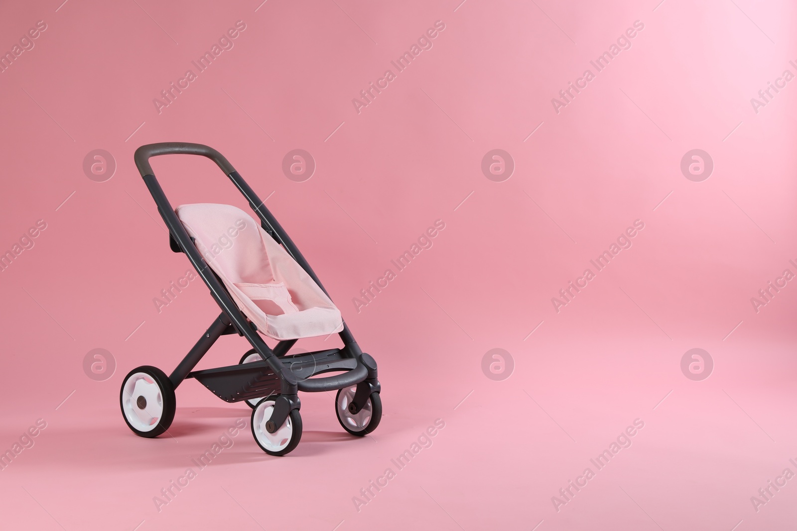 Photo of Stylish doll stroller on pink background, space for text. Kid's toy