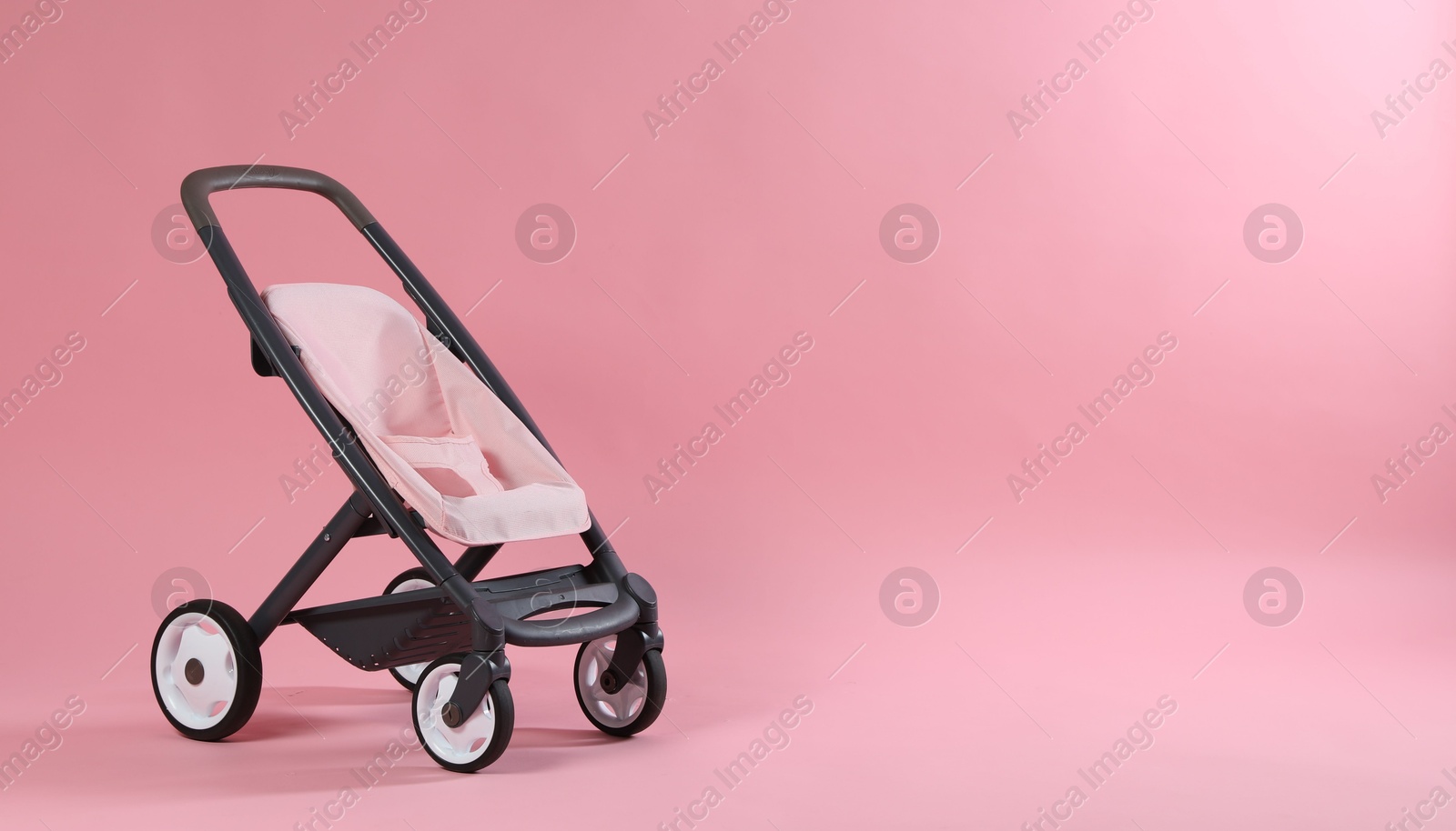 Photo of Stylish doll stroller on pink background, space for text. Kid's toy