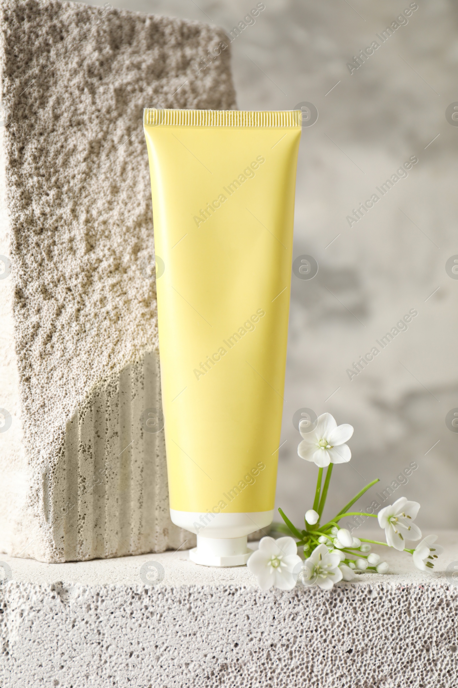 Photo of Tube of cream and beautiful white flowers on concrete block