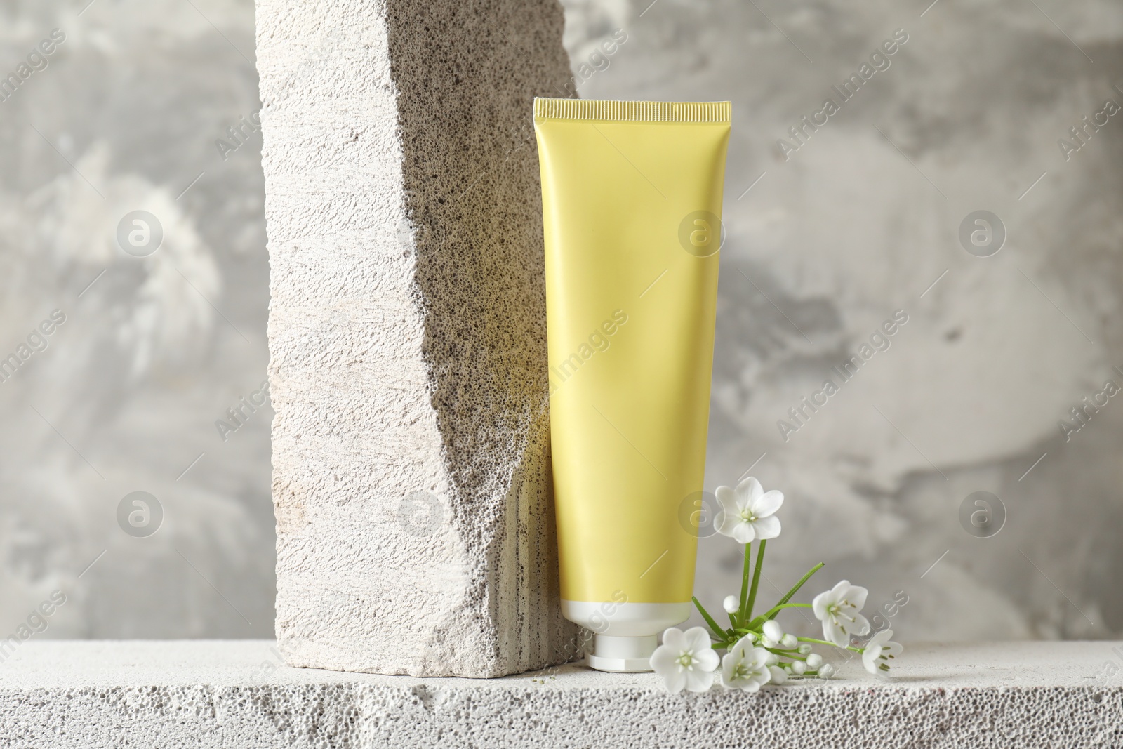 Photo of Tube of cream and beautiful white flowers on concrete block