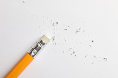 Photo of Pencil with eraser and scraps on white sheet of paper, top view