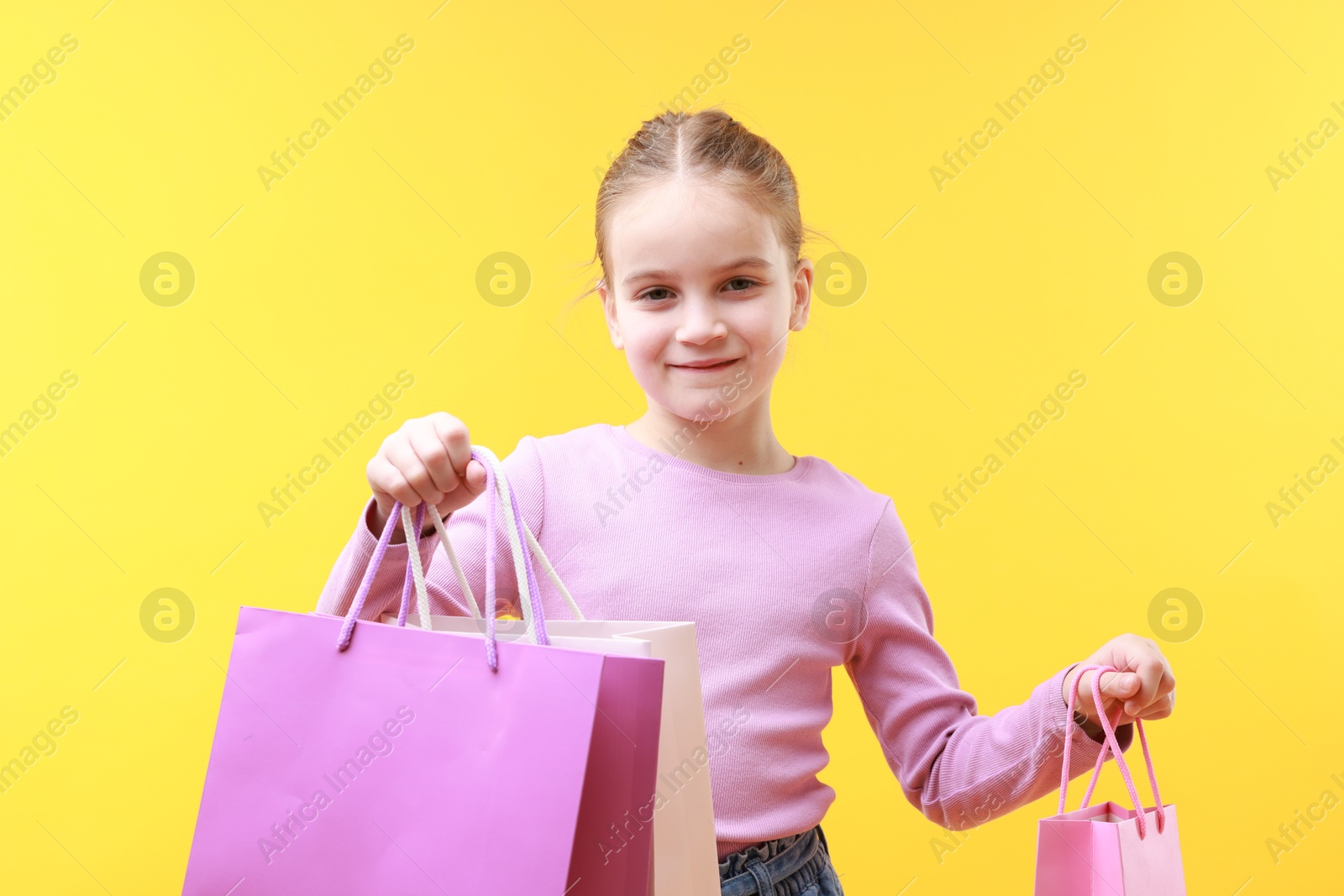 Photo of Cute little girl with shopping bags on yellow background