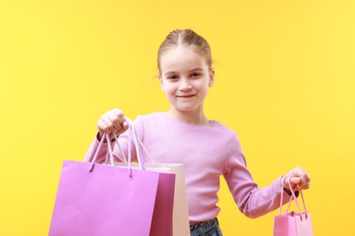 Cute little girl with shopping bags on yellow background