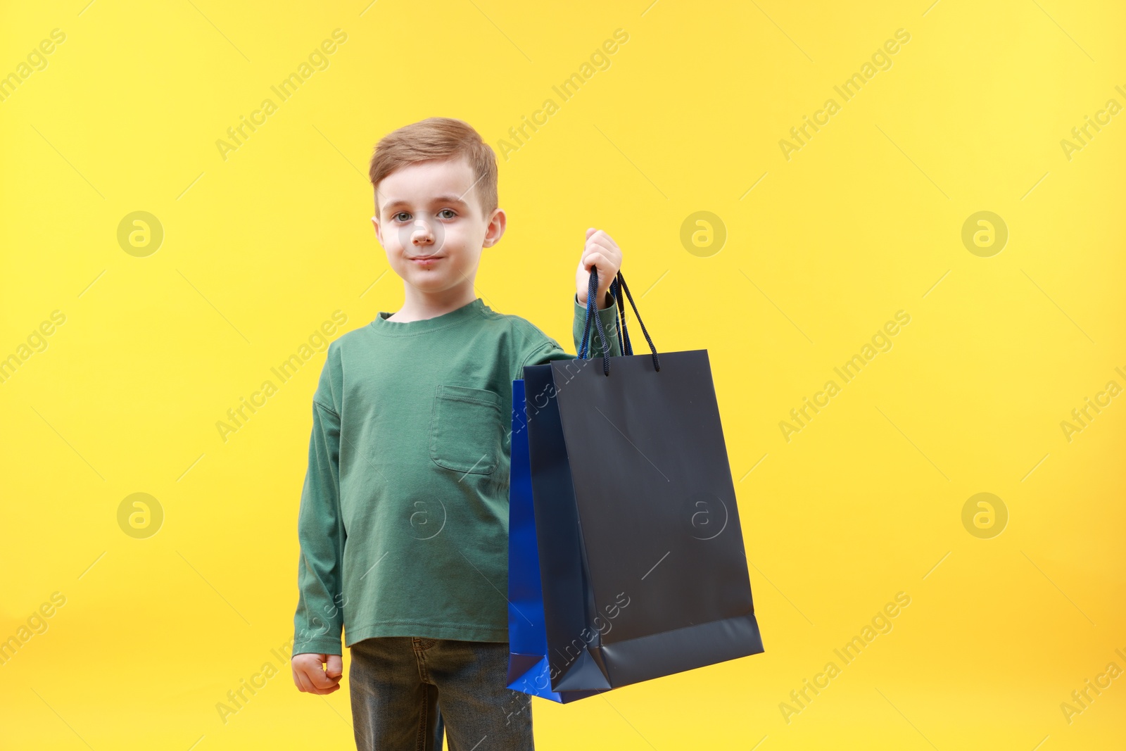 Photo of Cute little boy with shopping bags on yellow background