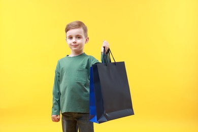 Cute little boy with shopping bags on yellow background