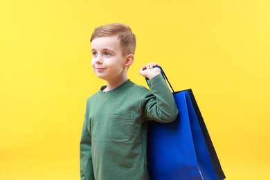 Cute little boy with shopping bags on yellow background