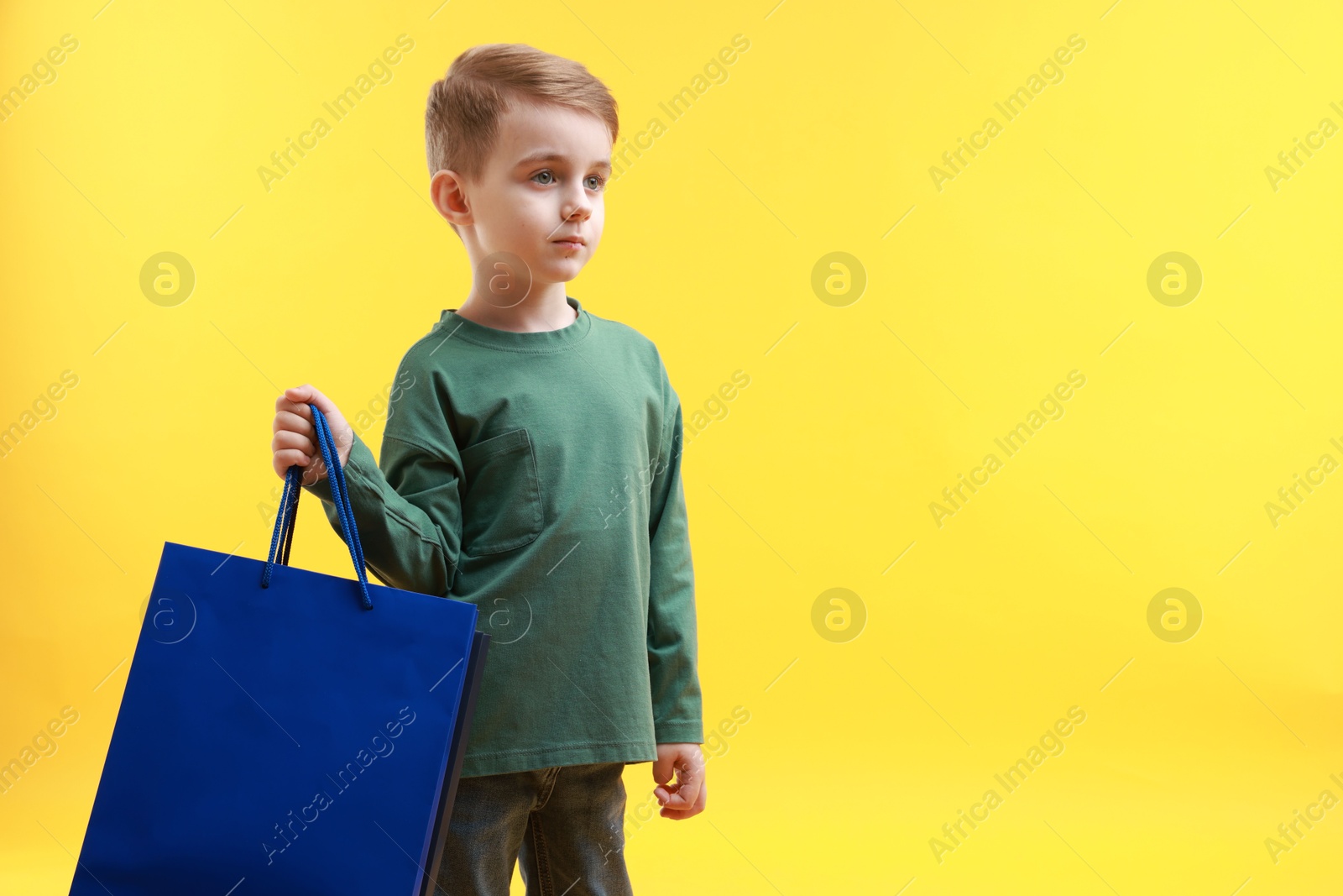 Photo of Cute little boy with shopping bags on yellow background. Space for text