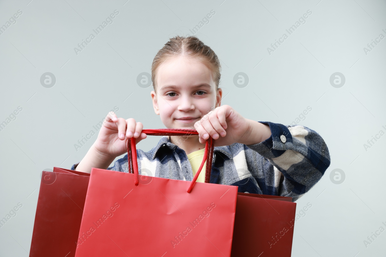 Photo of Cute little girl with shopping bags on grey background