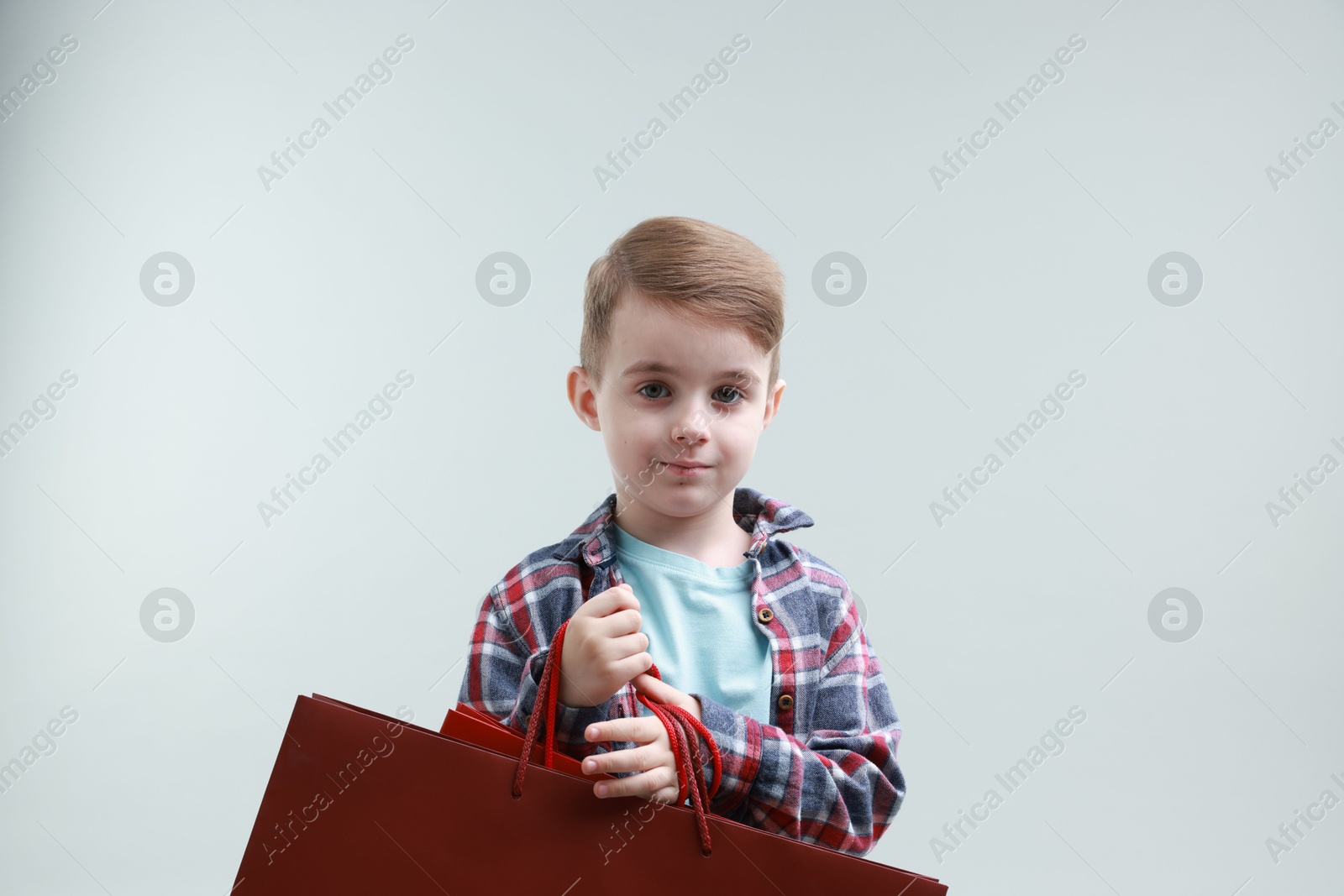 Photo of Cute little boy with shopping bags on grey background