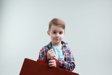 Cute little boy with shopping bags on grey background