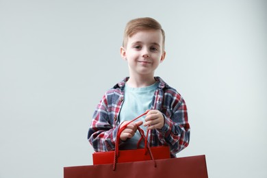 Photo of Cute little boy with shopping bags on grey background