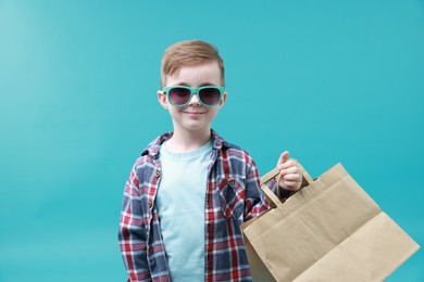 Photo of Cute little boy with shopping bags on light blue background