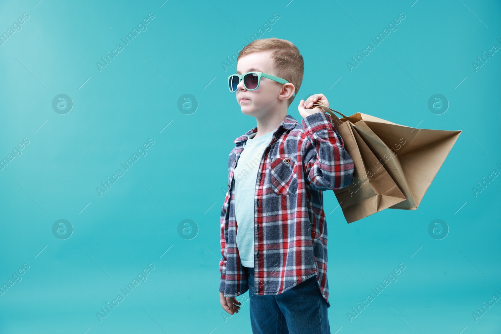 Photo of Cute little boy with shopping bags on light blue background. Space for text