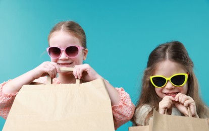 Happy little friends with shopping bags on light blue background