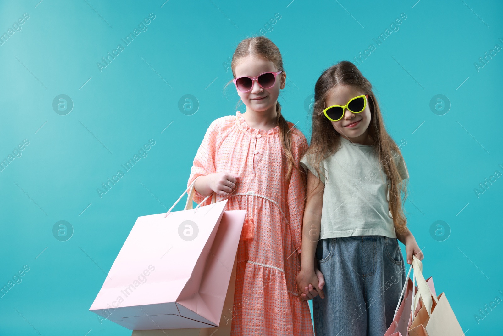 Photo of Cute little friends with shopping bags on light blue background. Space for text