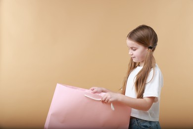 Cute little girl with shopping bag on beige background. Space for text