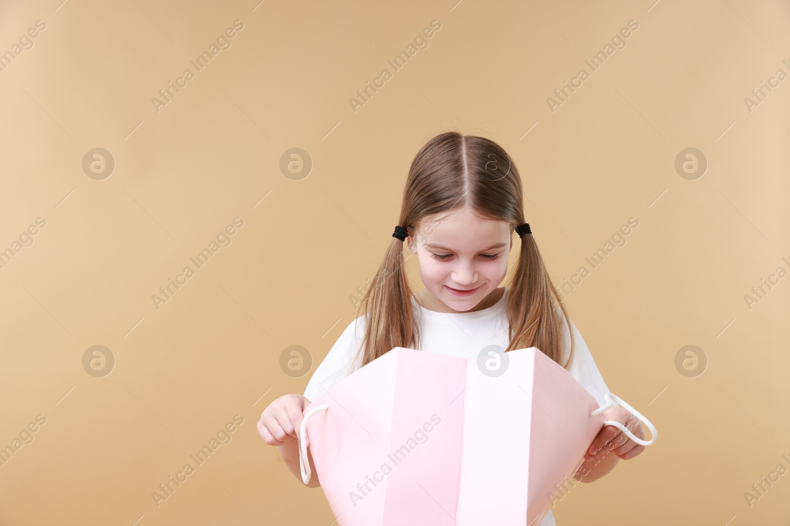 Photo of Cute little girl with shopping bag on beige background. Space for text