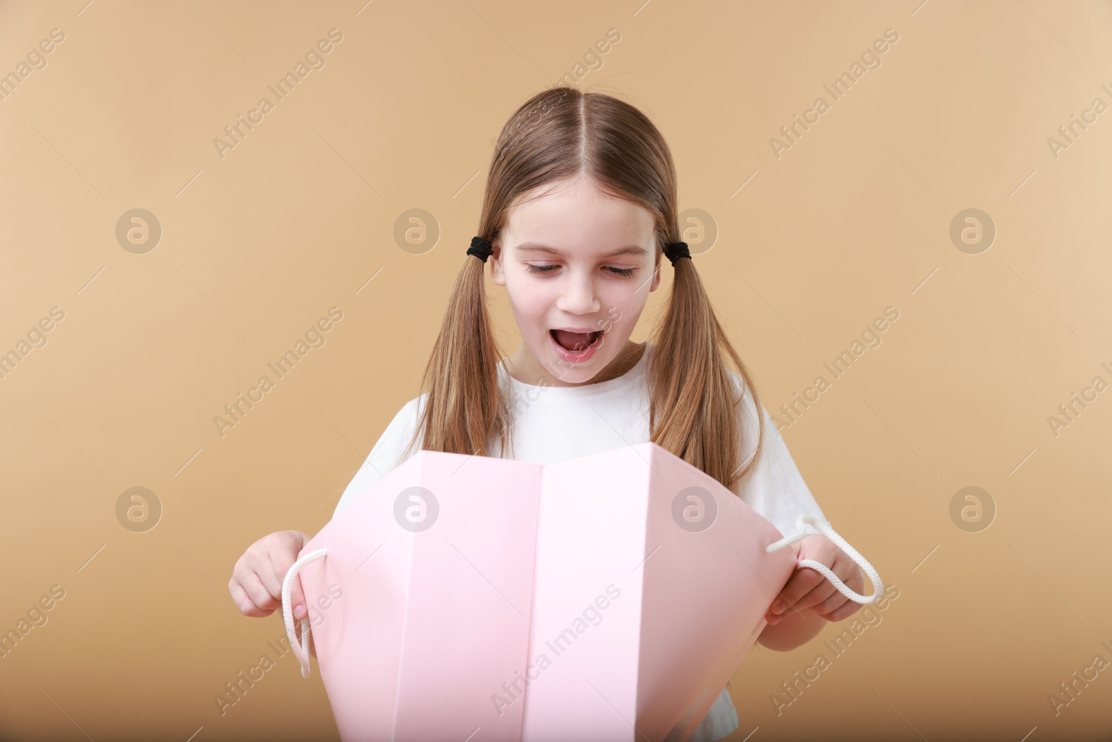 Photo of Cute little girl with shopping bag on beige background