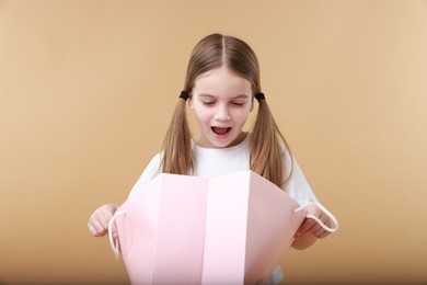 Cute little girl with shopping bag on beige background