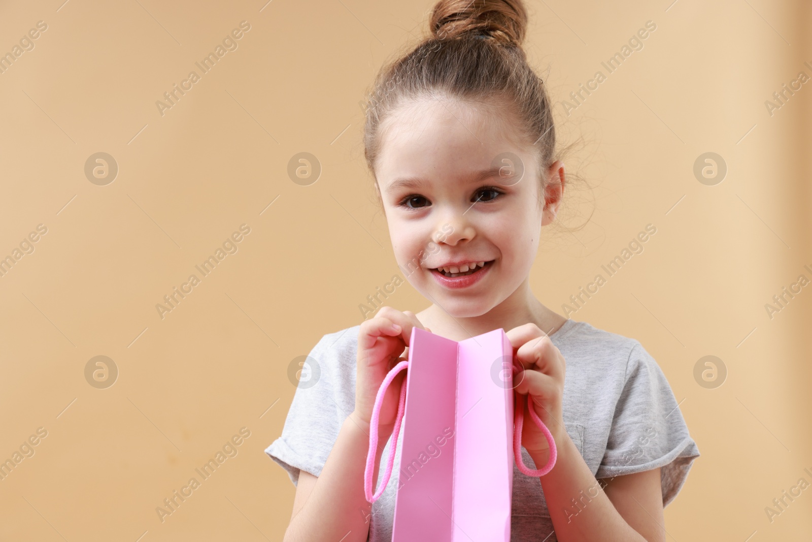 Photo of Happy little girl with shopping bag on beige background. Space for text