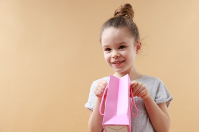 Photo of Happy little girl with shopping bag on beige background. Space for text