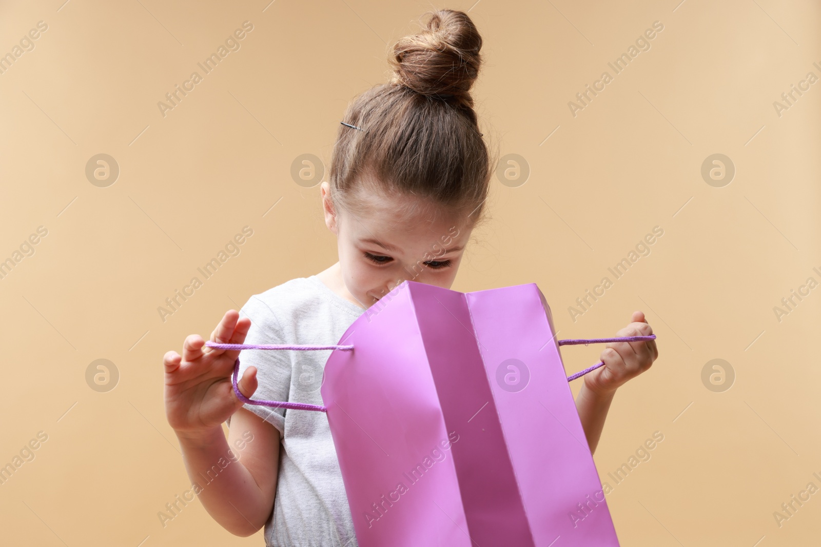 Photo of Cute little girl with shopping bag on beige background