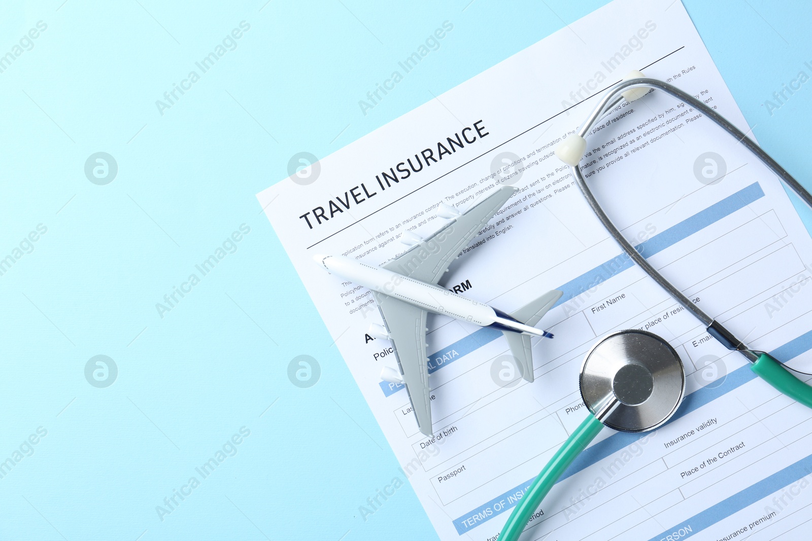 Photo of Medical tourism. Travel insurance application form, stethoscope and plane model on light blue background, flat lay. Space for text