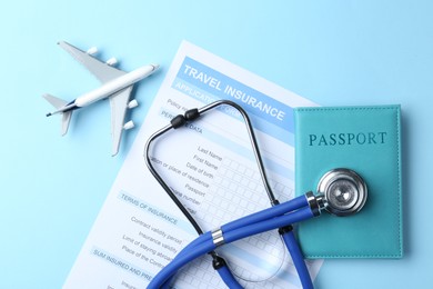 Photo of Medical tourism. Travel insurance application form, stethoscope, passport and plane model on light blue background, flat lay