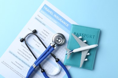 Photo of Medical tourism. Travel insurance application form, stethoscope, passport and plane model on light blue background, flat lay