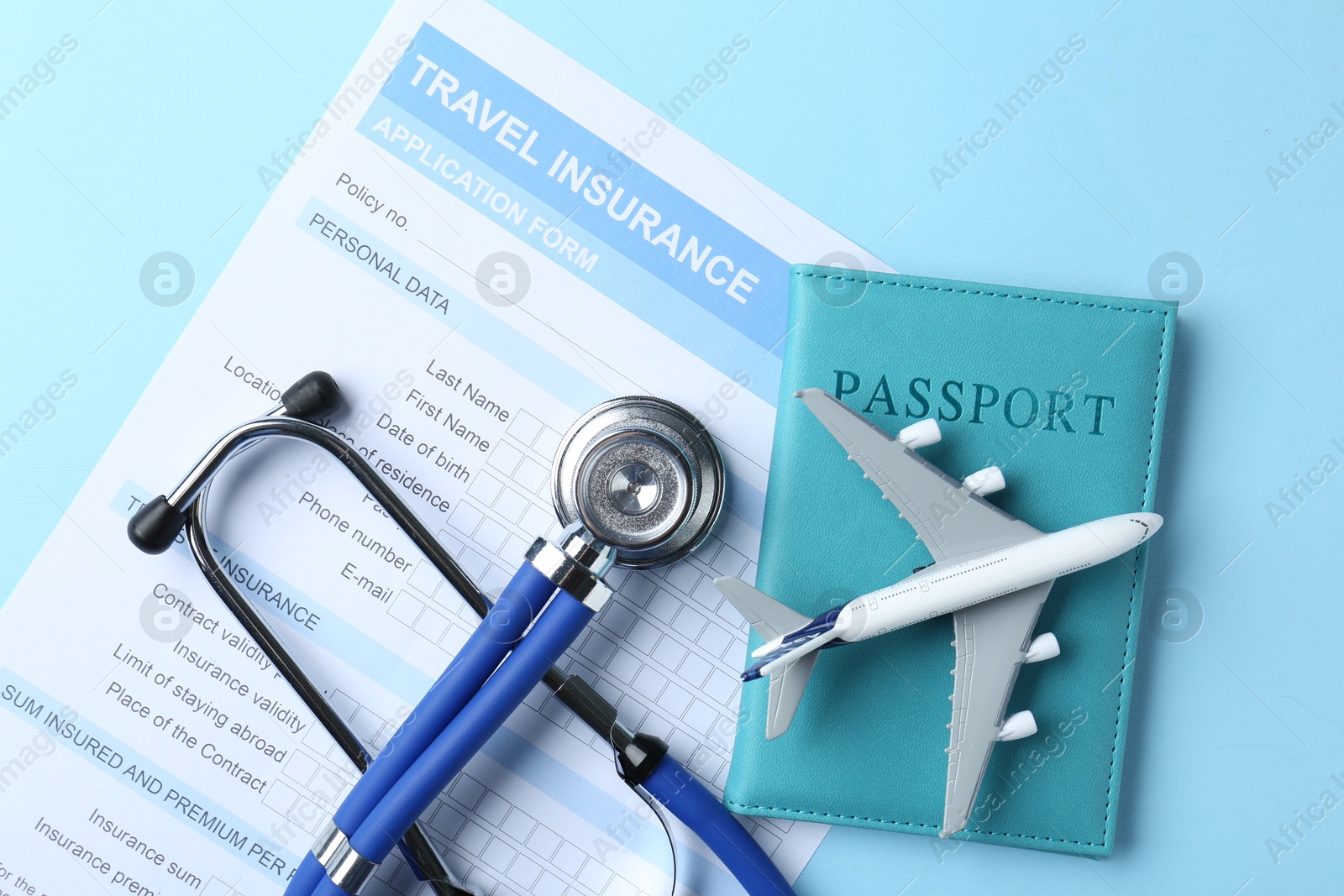 Photo of Medical tourism. Travel insurance application form, stethoscope, passport and plane model on light blue background, flat lay