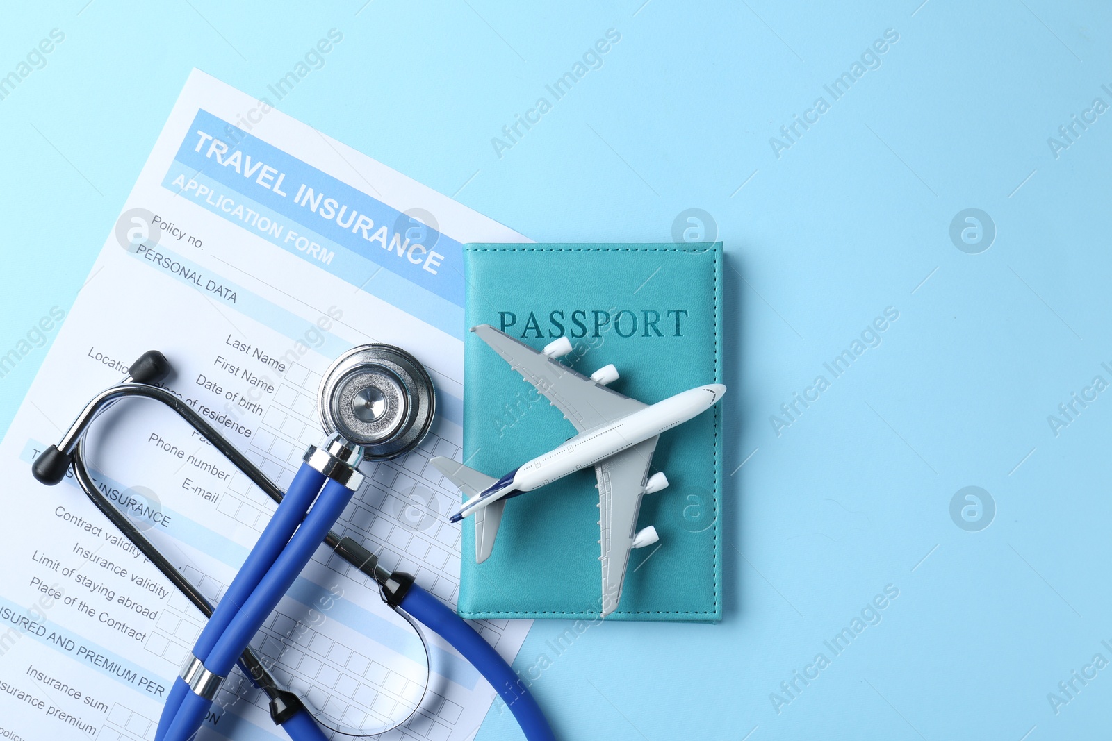 Photo of Medical tourism. Travel insurance application form, stethoscope, passport and plane model on light blue background, flat lay. Space for text