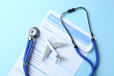 Photo of Medical tourism. Travel insurance application form, stethoscope and plane model on light blue background, flat lay