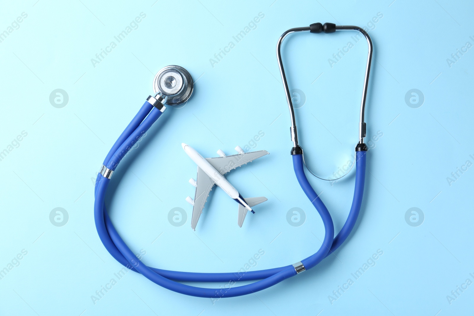 Photo of Medical tourism. Stethoscope and plane model on light blue background, top view