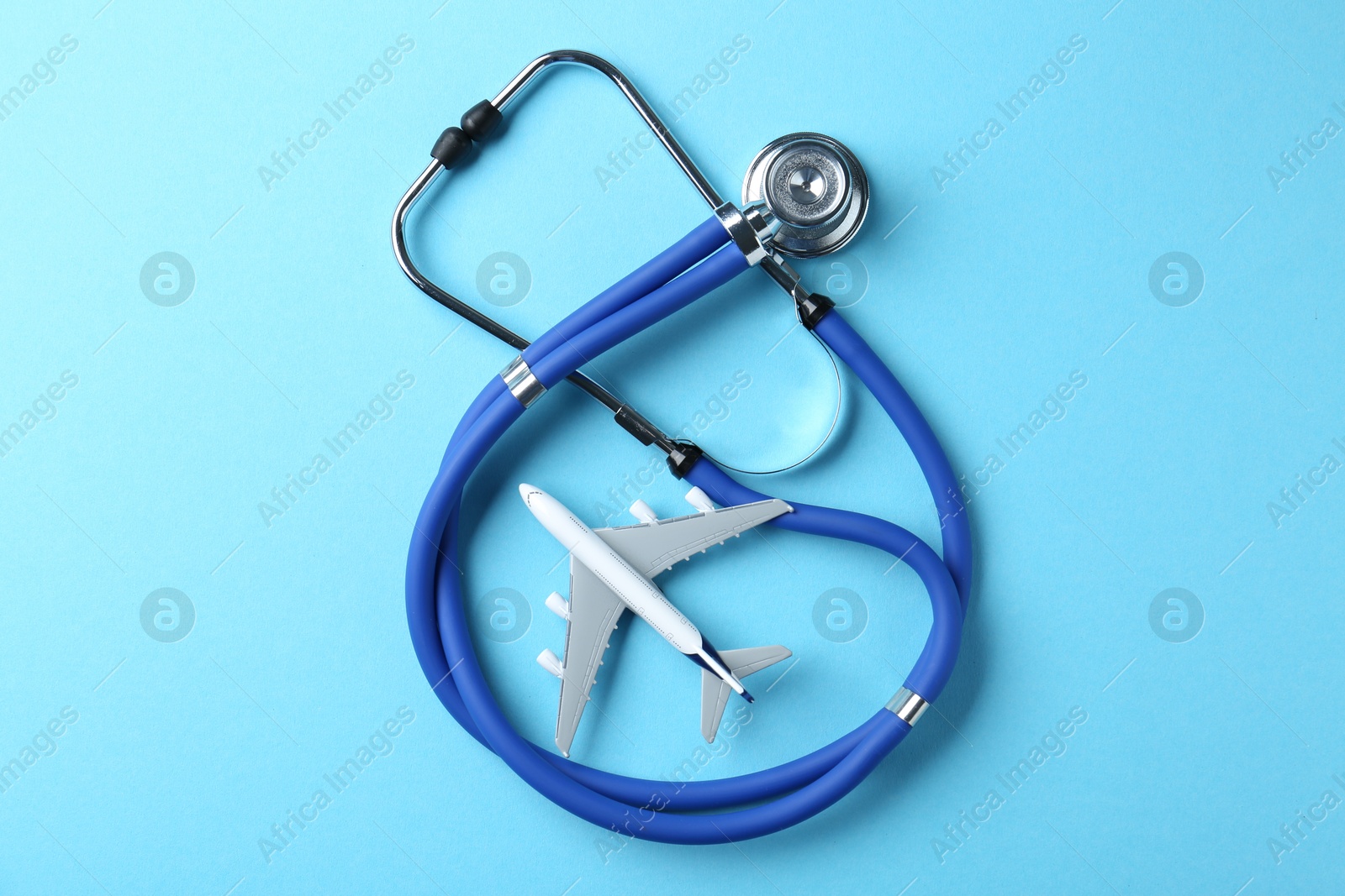 Photo of Medical tourism. Stethoscope and plane model on light blue background, top view