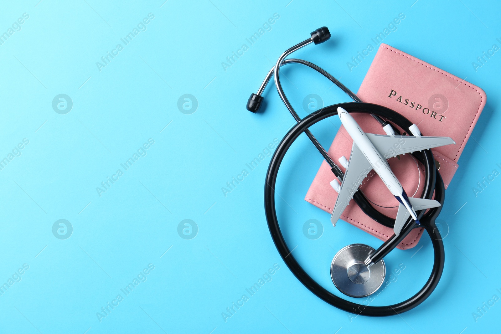 Photo of Medical tourism. Stethoscope, passport and plane model on light blue background, top view. Space for text