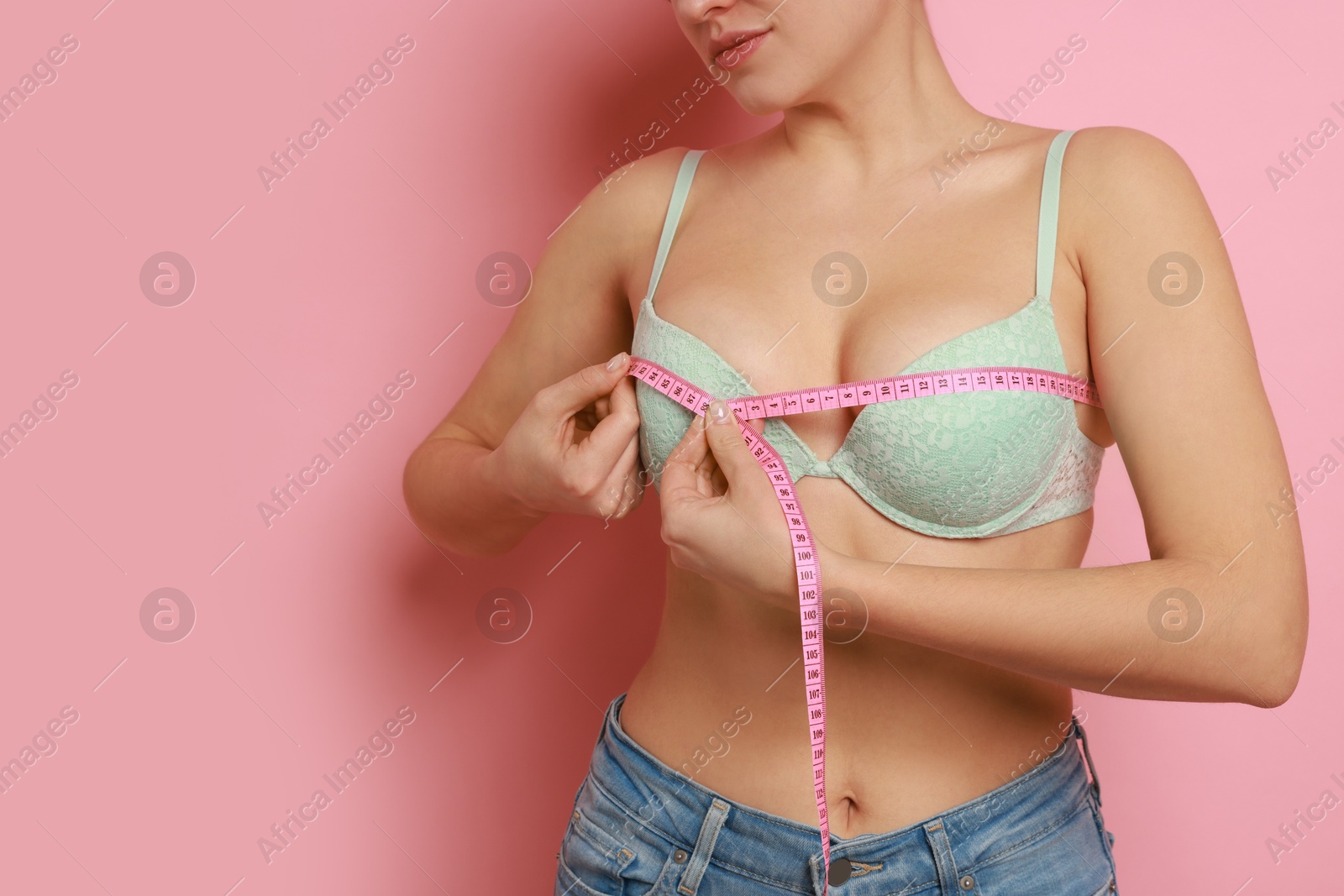 Photo of Woman in beautiful bra measuring breast circumference on pink background, closeup. Space for text