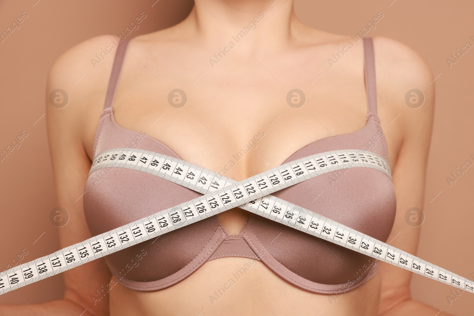 Photo of Woman in beautiful bra measuring breast circumference on beige background, closeup