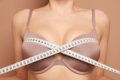 Photo of Woman in beautiful bra measuring breast circumference on beige background, closeup